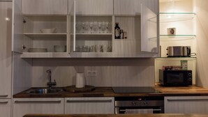 Una cocina moderna con armarios blancos, microondas integrado y repisa de vidrio con copas y botellas de vino.