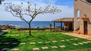 A coastal property with a clear view of the sea, a well-maintained lawn, and a stone pathway leading to a wooden structure.