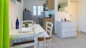 A compact kitchen with a dining area, a small refrigerator, and a TV mounted on the wall.
