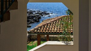 A view from a balcony overlooking a rocky coastline with a tiled roof and a stone wall.
