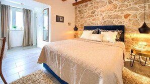 A bedroom with a stone wall, a bed with a blue headboard, and a wooden ceiling.