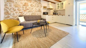 A modern living room with a stone wall, a sofa, a yellow armchair, a coffee table, and a kitchen area with white cabinets and a microwave.