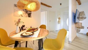 A dining area with a round table, yellow chairs, a woven pendant light, and a wall-mounted TV.