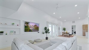 Uma sala de estar ampla com um sofá seccional grande, uma TV de tela plana na parede e uma área de jantar com mesa e cadeiras.