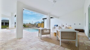 Um pátio moderno ao ar livre com piscina, mobiliário branco e vista para um prédio azul ao fundo.