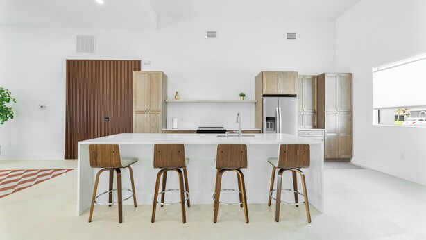 Uma cozinha moderna com ilha central, banquetas e armários de madeira.