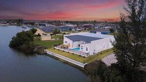 Uma casa moderna com um deck espaçoso e piscina, cercada por um lago e outras residências.