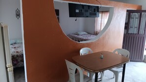 A room with a curved wall, a bed with a patterned bedspread, a small table with chairs, and a window with curtains. - Quinta "Los Tercos (Santiago)