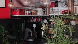 A modern kitchen with red walls, black countertops, and hanging pendant lights. There is a potted plant on the counter and a bowl of fruit. - Quiet village center and seaside T2 apartment with swimming pool and private parking. (Fréjus)
