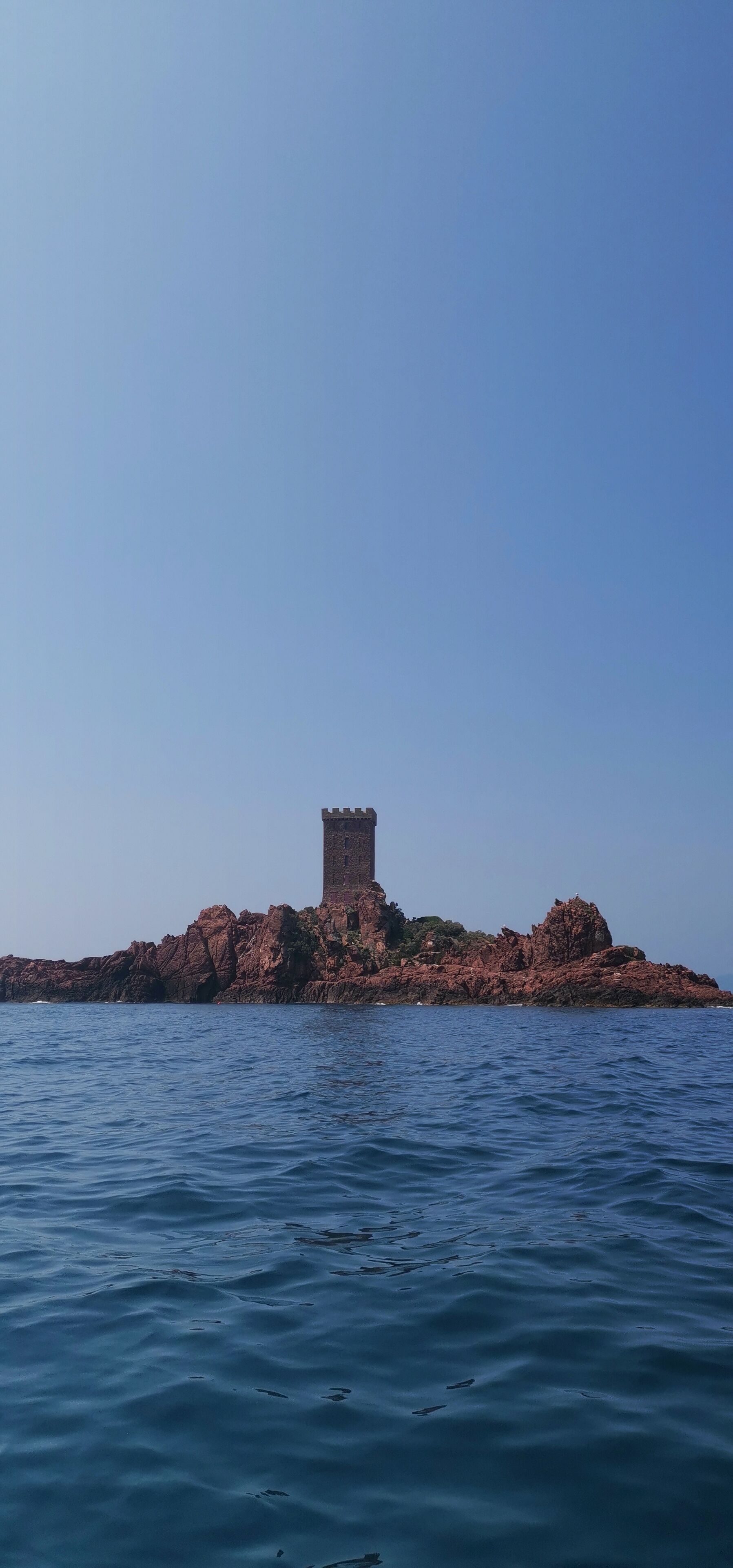 A coastal view with a rocky island featuring a single tower structure.