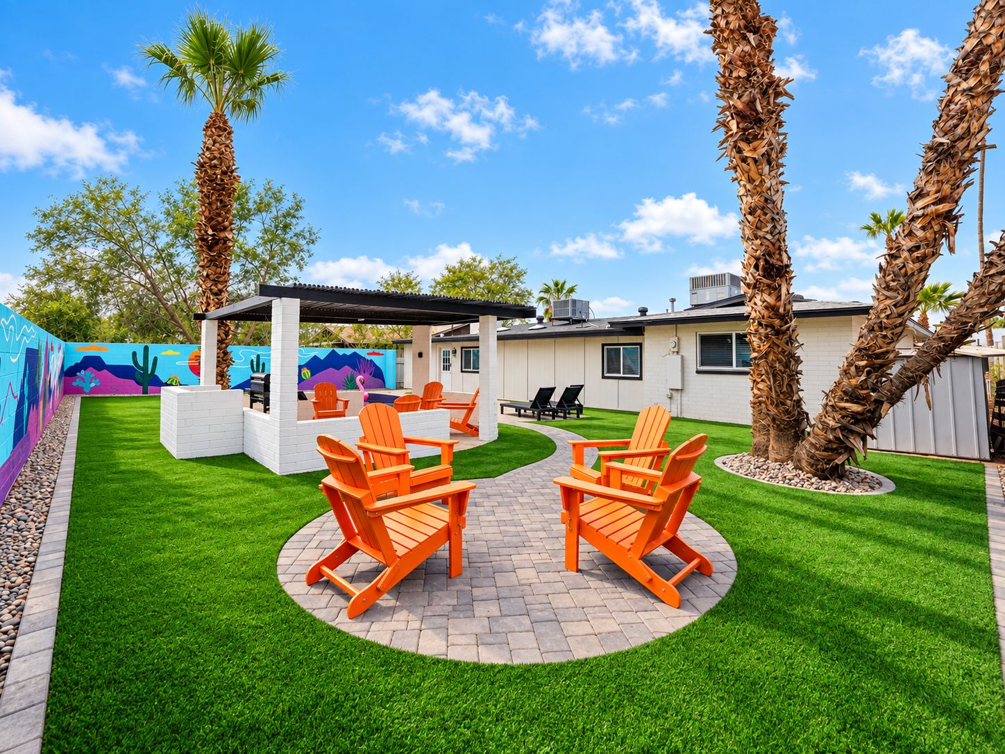 A backyard with a patio area, outdoor furniture, and a mural on the wall.