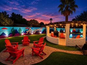 A patio area with red Adirondack chairs, a barbecue grill, and a poolside seating area.