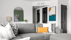 A modern living room with a grey sectional sofa, a glass coffee table, and a mirror on the wall.
