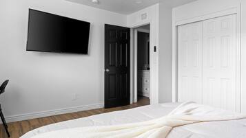 Un dormitorio con cama, televisor montado en la pared y puerta de acceso a un baño.