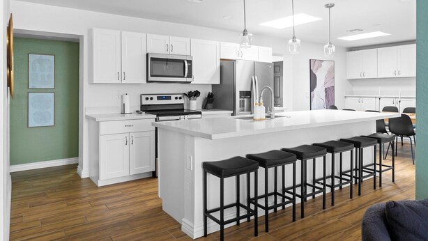 A modern kitchen with white cabinets, a central island with bar stools, stainless steel appliances, and pendant lighting.