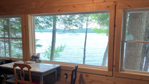 A cabin with wooden walls and large windows overlooking a lake. - Cozy cottage in charming Lincoln, ME with AC (Lincoln)
