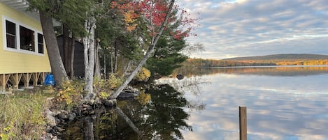 A lakeside cabin with a dock extending into the water, surrounded by autumn foliage.