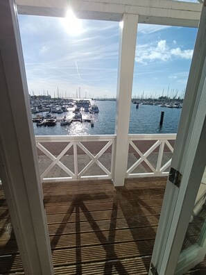 Una terraza de madera con vista a un puerto deportivo lleno de barcos y un puente al fondo.