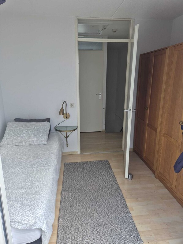 Un dormitorio con cama, una mesita de noche pequeña, un armario y una puerta que da a otra habitación.
