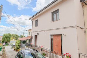 A two-story building with a light pink facade, a red door, and a small balcony with red flowers. - The Stars - Frigento (Frigento)