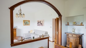 A room with a wooden dining table, a white sofa, a wooden cabinet, and a mirror with an arch. - Ca di Borra - Bio Garden & Stunning Views (Badia Tedalda)