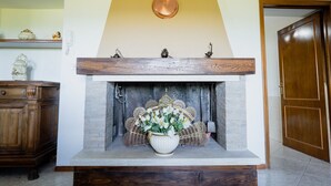 A fireplace with a white vase of flowers, a wooden mantel, and a copper pot hanging above. - Ca di Borra - Bio Garden & Stunning Views (Badia Tedalda)