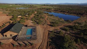 Vista aérea de uma propriedade com piscina, um amplo campo aberto e um lago.