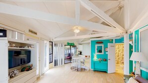 A spacious living area with a television, a dining table, and a kitchen area with teal cabinets.