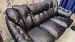 A black leather sofa with a tufted design, positioned against a floral wallpaper background. - Luxury stay on budget (Kolkata)