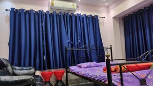 A bedroom with a bed, a black leather chair, two red stools, and blue curtains. - Luxury stay on budget (Kolkata)
