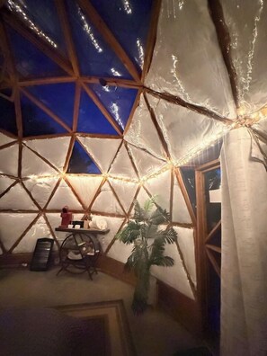 Une structure en forme de dôme géodésique avec une ossature en bois, une petite table sur laquelle sont posés divers objets, et une plante.