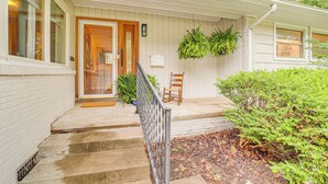 Een huis met een veranda, een houten deur, een klein zitgedeelte en een raam.