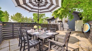 An outdoor patio with a table set for four, surrounded by wooden chairs, under a striped umbrella. - Walk to Dtwn: Cozy Home w/ Fireplace in Charlevoix (Charlevoix)