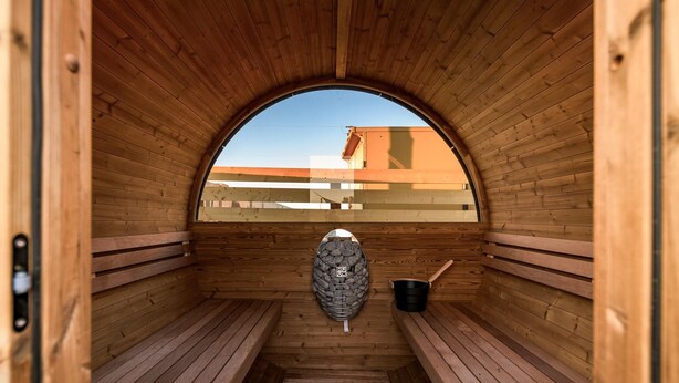 A sauna with wooden benches, a stone wall, and a view of buildings outside. - Airstream w/ Private Hot Tub (Unit D) - 3 Person Airstream with Private Hot Tub (Williams)