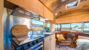 A compact kitchen with a stove, sink, and wooden cabinets. - Airstream w/ Private Hot Tub (Unit D) - 3 Person Airstream with Private Hot Tub (Williams)