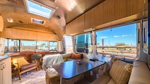A well-lit RV interior with a dining area, seating, and large windows offering views of the outside. - Airstream w/ Private Hot Tub (Unit D) - 3 Person Airstream with Private Hot Tub (Williams)