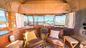 A cozy RV interior with two leather chairs, a small table, and a window offering a view of the outside. - Airstream w/ Private Hot Tub (Unit D) - 3 Person Airstream with Private Hot Tub (Williams)