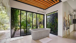 A modern bathroom with a freestanding bathtub, large windows, and a view of lush greenery.