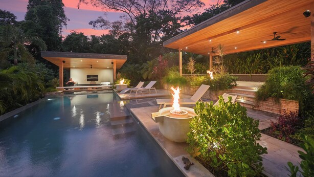 A modern outdoor pool area with lounge chairs, a fire feature, and a covered seating area.