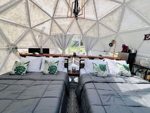 A geodesic dome tent with two beds, a table, and a hanging light fixture.