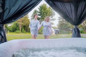 Two people walking towards an outdoor hot tub area with a gazebo in the background.