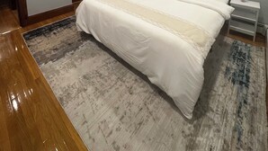 Quarto com uma cama grande, mesa de cabeceira, janela com cortinas e piso de madeira.