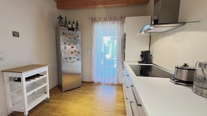 A compact kitchen with a refrigerator, a coffee maker, and a small table with wine bottles.