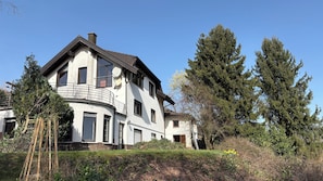 A two-story house with a balcony, large windows, and a chimney.