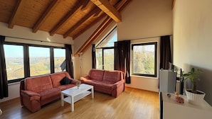 Un amplio salón con dos sofás, una mesa de centro y grandes ventanas que ofrecen vistas al campo.
