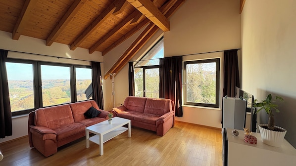 A spacious living room with two sofas, a coffee table, and large windows offering a view of the countryside.