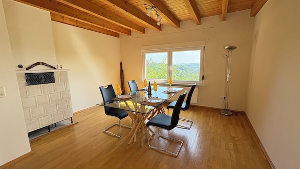 Un comedor con una mesa de vidrio, sillas negras y vistas a la vegetación a través de amplios ventanales.