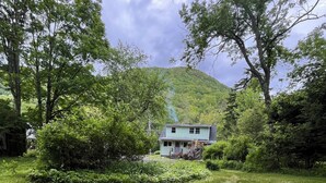 A house surrounded by lush greenery and a stone fire pit in the foreground.