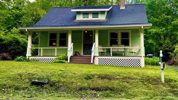 A green house with a porch, a chimney, and a mailbox.