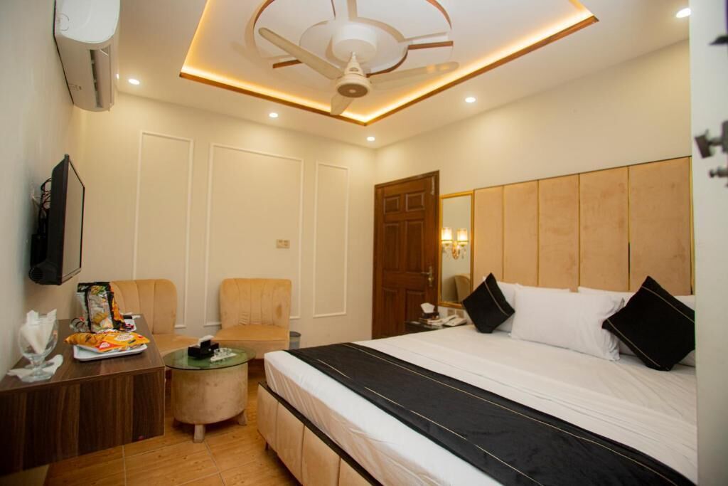 A hotel room with a bed, a desk, a chair, a small table, and a ceiling fan.